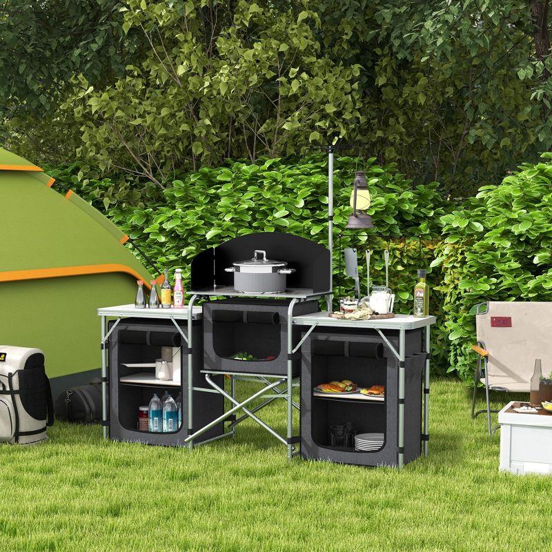 Outsunny Camping Kitchen Table, Portable Folding Camp Kitchen, Aluminum Cook Station with 3 Fabric Cupboards, Windshield, Carrying Bag, Black